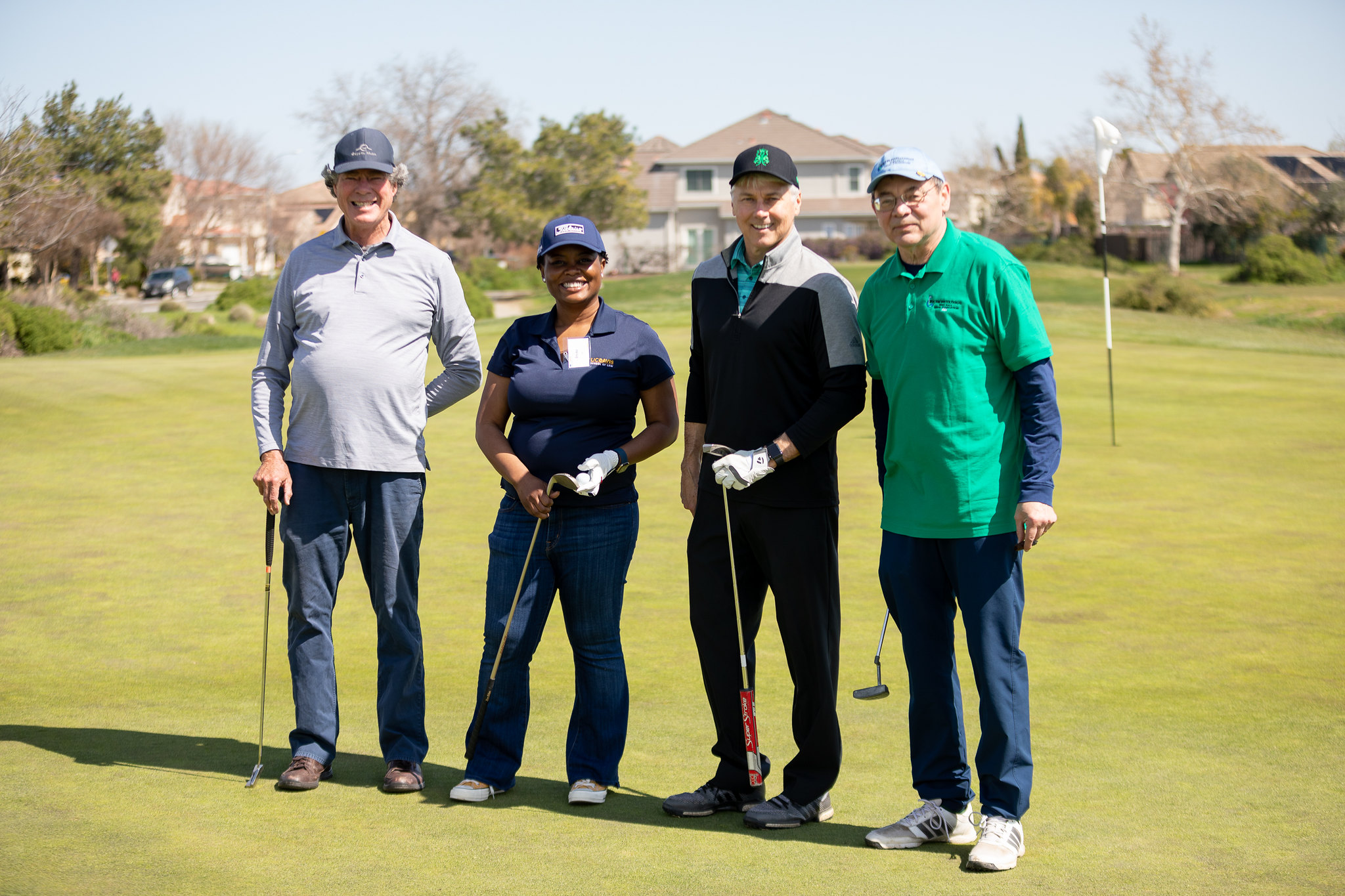 Four people stand together on a golf course.