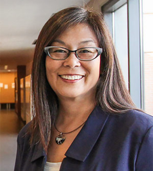 Elizabeth Inadomi wearing eyeglasses and a suit jacket. She is brightly smiling at the camera.