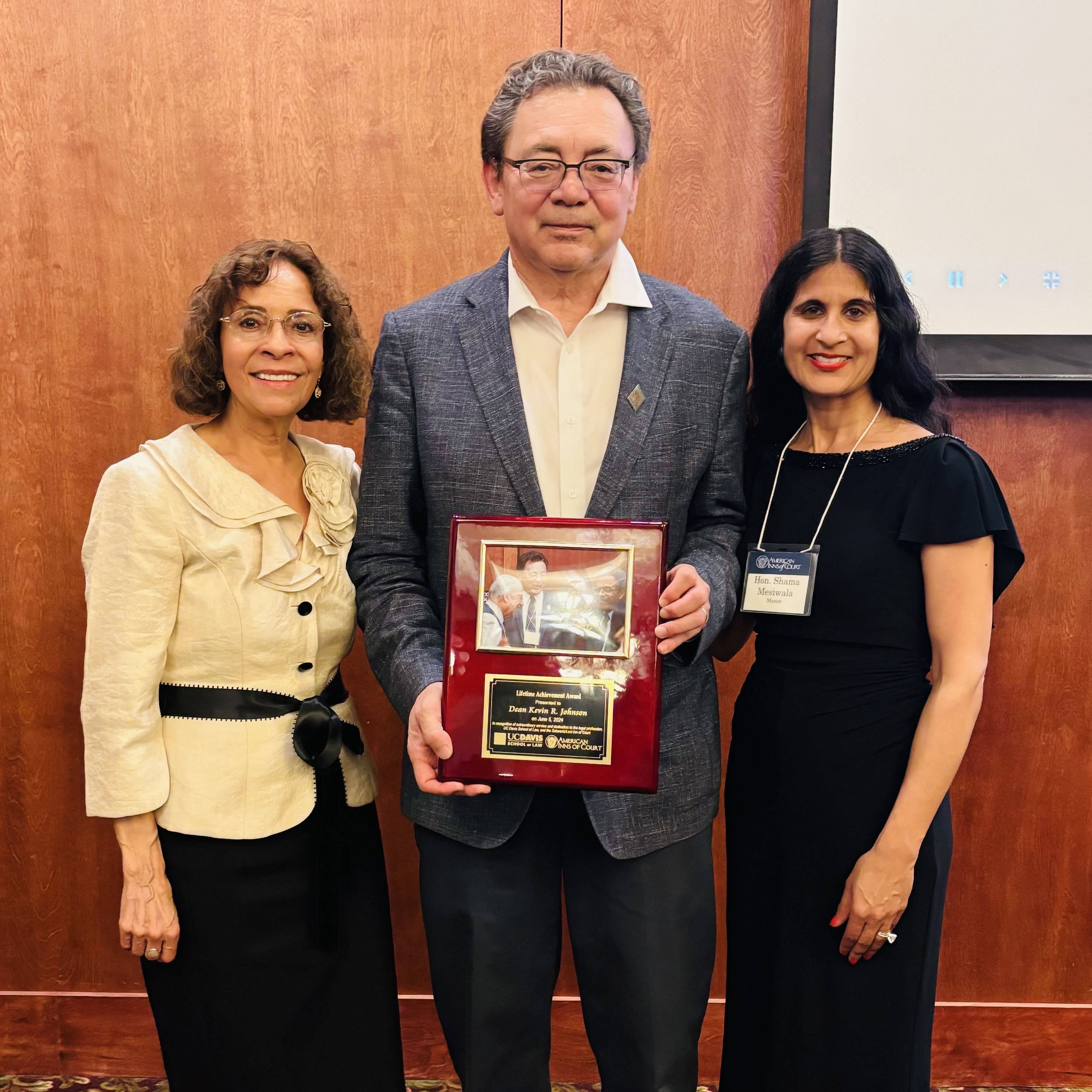 UC Davis Law Dean Kevin Johnson is wearing a gray suit and holding the Schwartz/Levi Inn of Court’s Lifetime Service Award. To the left of him is the retired Sacramento Superior Court Judge Emily E. Vasquez and to the right is California Court of Appeal, Third Appellate District Justice Shama Hakim Mesiwala ’98.