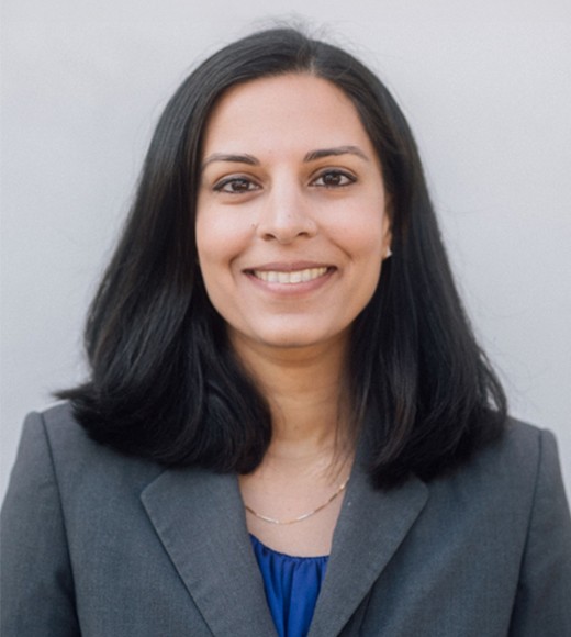 UC Davis Law Professor Nila Bala wearing a grey suit and blue blouse, she is smiling.