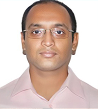 A close-up of a man wearing a blush shirt and glasses.