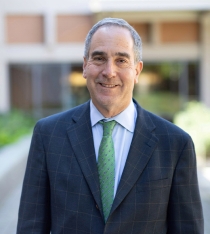 David Sandino wearing a suit with a green tie. He is standing outside in the King Hall courtyard and is smiling at the camera.