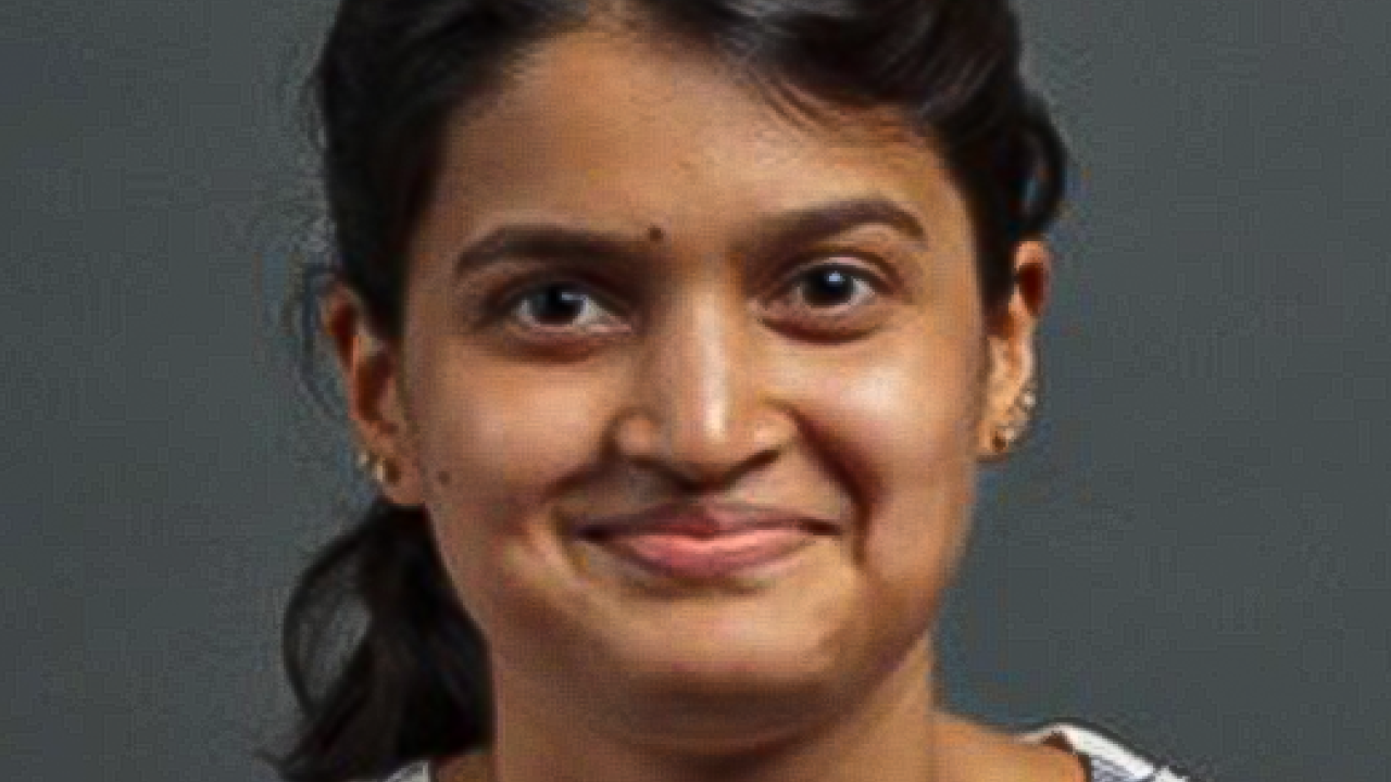 Smiling young woman with dark hair in a checkered shirt against a gray background.