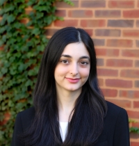 Mahi Taban, a KHOP graduate, wearing a suit and posing in front of a brick wall.