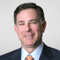 Smiling man in navy suit and orange tie, studio headshot