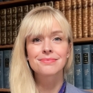 Acting Professor of Law Sarah Polcz wearing a blue blazer and standing in front of a bookshelf.